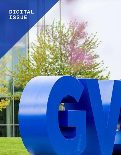 Large blue letters spelling GV take up most of the frame, trees with spring leaves and flowers in the background and in the distance the windows of the Mary Idema Pew Library. Text at the top left reads "DIGITAL ISSUE"