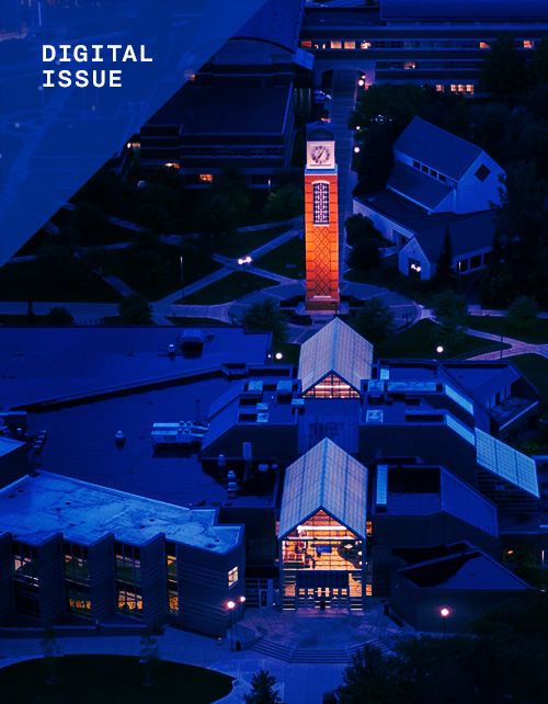 An arial drone shot of the GVSU campus with a dark blue tint. Only the clocktower and the inside of buildings glow orange, including the Kirkhof Center. Text in the top left reads "DIGITAL ISSUE."