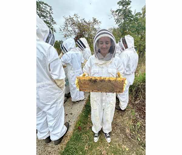 people in white beekeeper suits, one person in front holding a hive