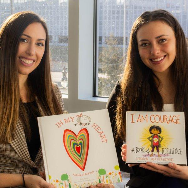 two women seated next to each other holding children's books