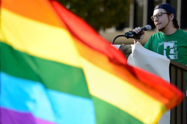 rainbow flag in front of person at podium with microphone