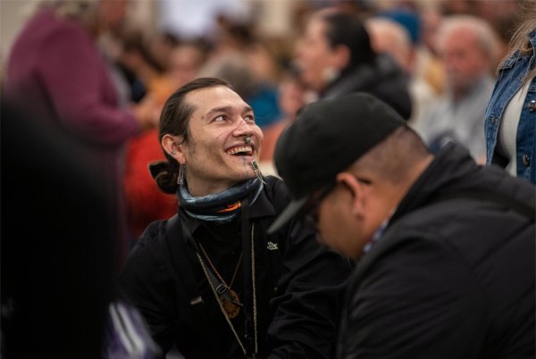Grand Valley student Nbiish Kenwabikise, left, laughs with others before playing in a drum circle in preparation for author Robin Wall Kimmerer to take the stage.