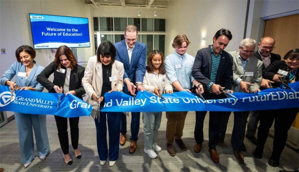 Several people cut into a ribbon with the Grand Valley State University logo and the words "Grand Valley State University futureEDlab." A screen behind them says, "Welcome to the Future of Education!" "Blue Dot" and "futureEDlab." The GVSU logo is also on the screen.