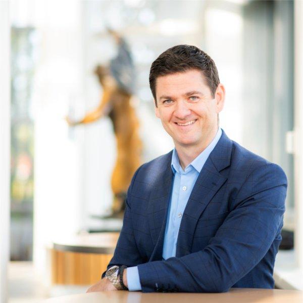 Miloš Topić with arm resting on table, sculpture behind him, he is dressed in blue suit jacket and light blue shirt