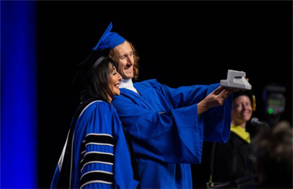 A graduate takes a selfie with President Mantella as he crosses the stage at Commencement.
