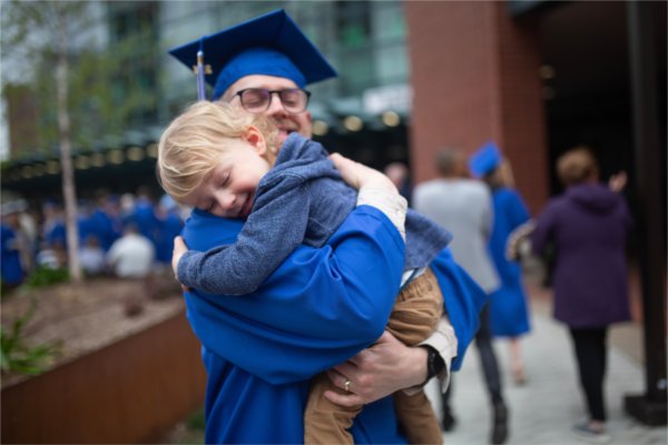 A graduate hugs a young child tight following Commencement ceremonies. 
