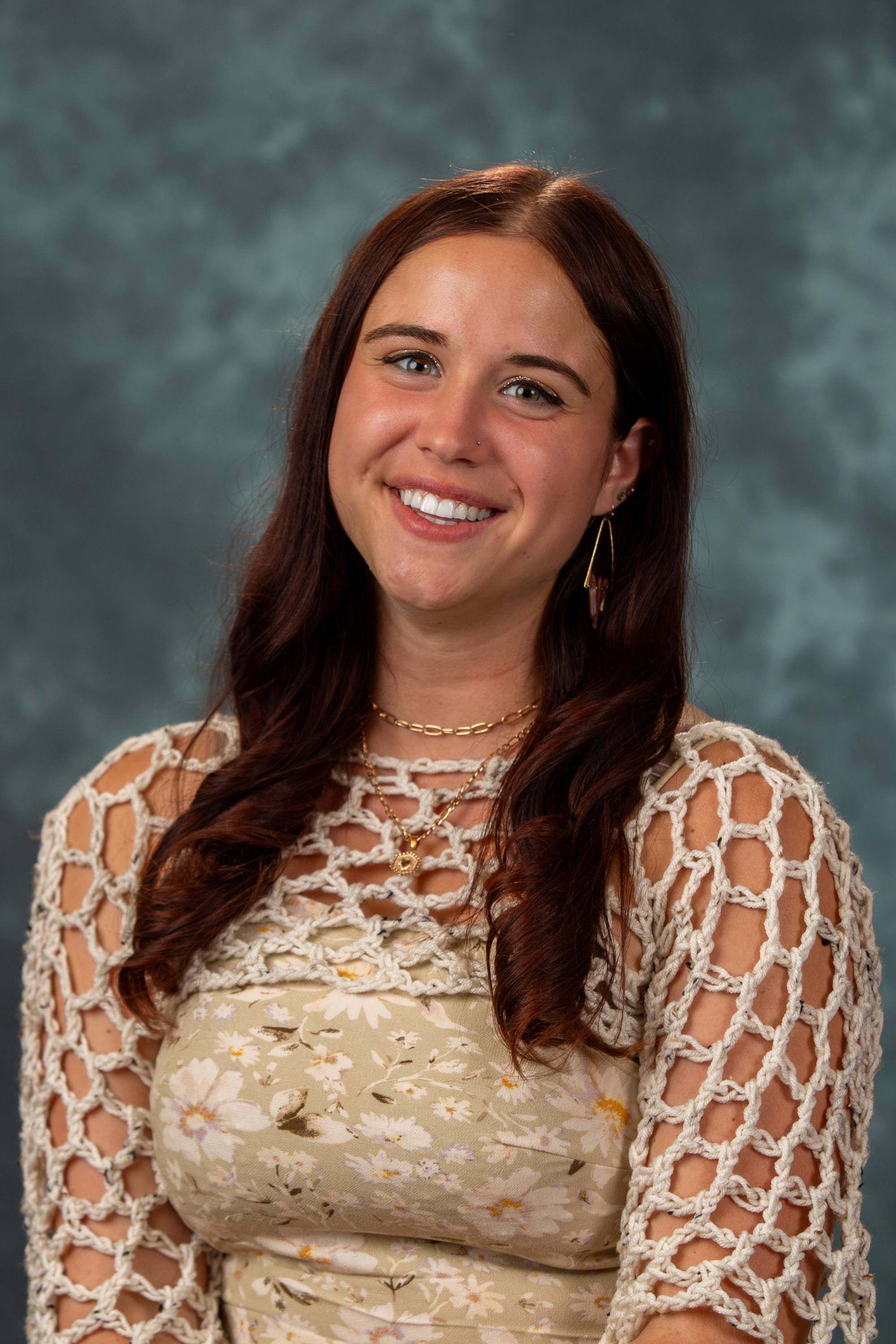 Annah Strang wearing a checkered blazer, a white turtleneck and smiling in front of a black curtain