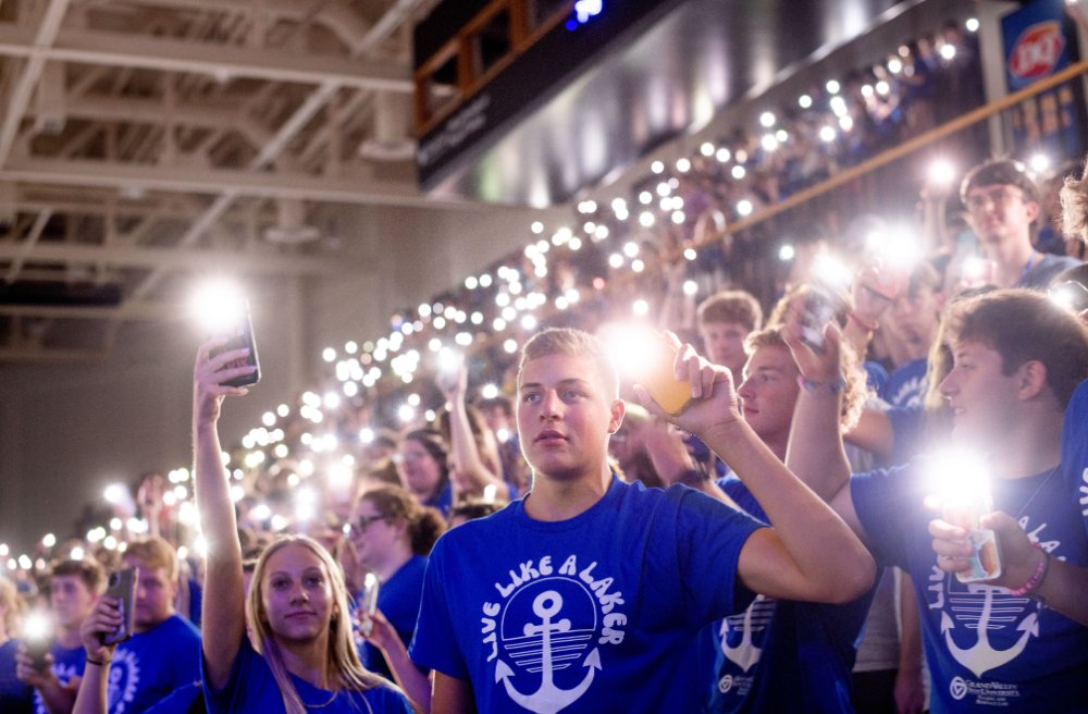 Students wearing blue shirts holding up their cell phones with flashlights on