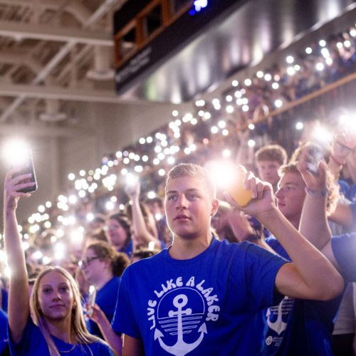 Students wearing blue shirts holding up their cell phones with flashlights on