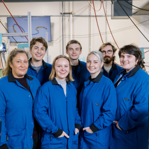 group of seven people standing in blue lab coats in a workshop