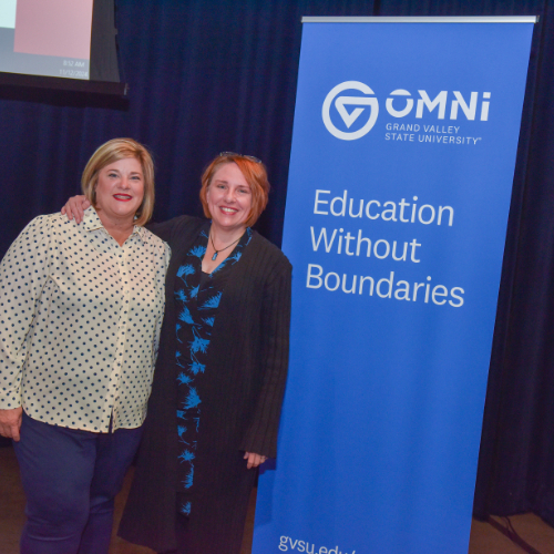 two people standing next to vertical banner for Omni from GVSU, Education Without Boundaries