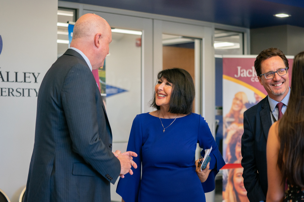 President Mantella in center talks with Jackson College President Daniel Phelan, two vertical banners for GVSU and Jackson College are in the background