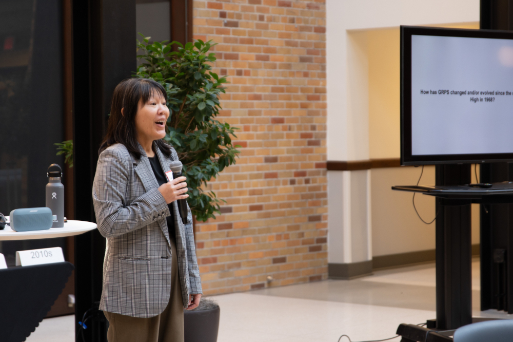 Leanne Kang stands with microphone, screen off to right side