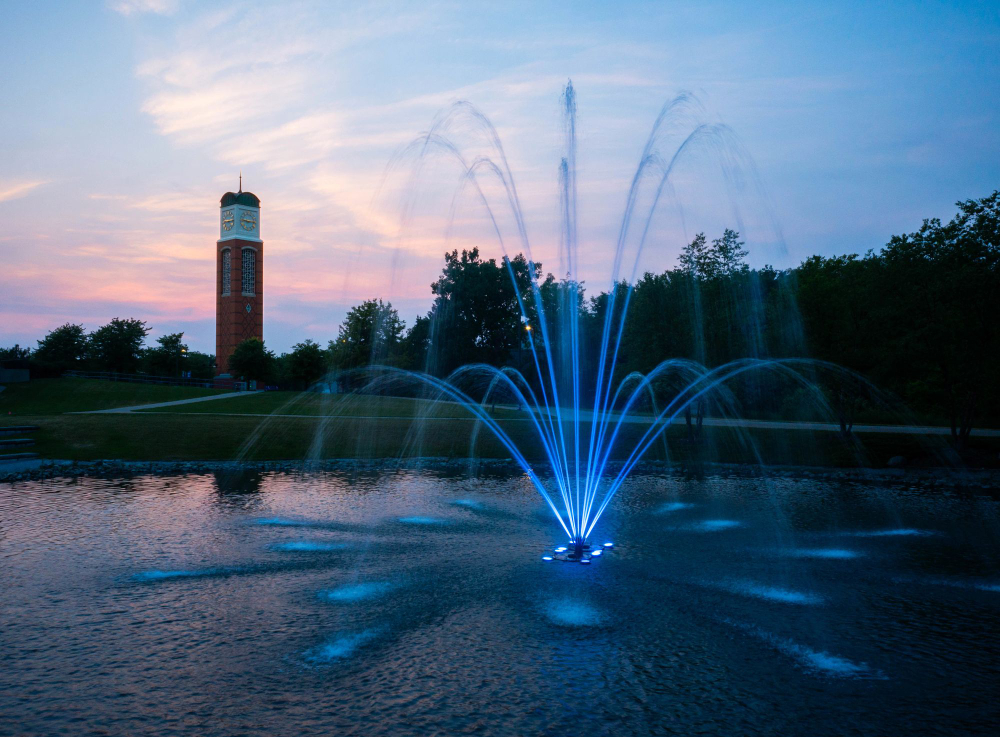 sunset photo of the carillon tower in background with fountain at Zumberge pond lit up in blue