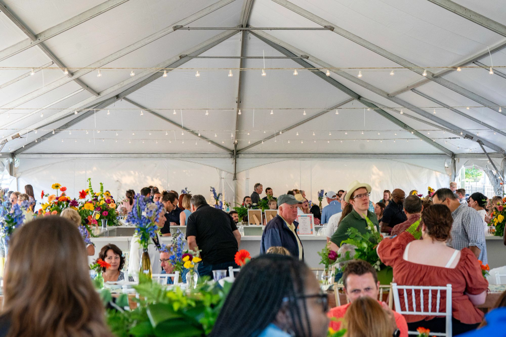 under white tent, many people seated at round tables