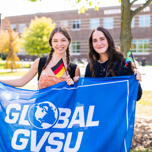 two students hold Global GVSU flag in front of Kirkhof Center