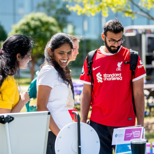 3 students look at a tabling event outside on the Kirkhof Center lawn