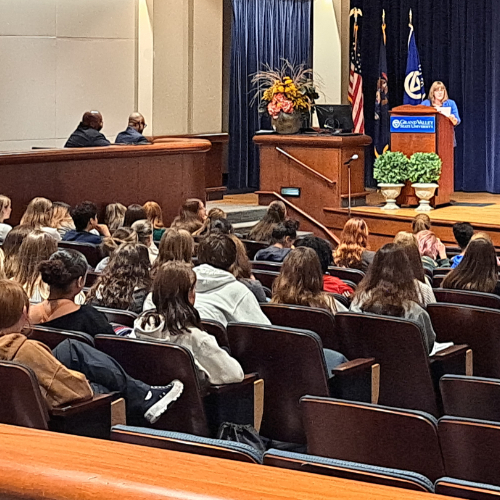 Amy Schelling speaks in Loosemore Auditorium, people seated in audience in rows