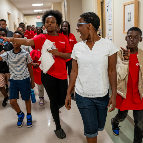 faculty member in white shirt and shorts leads a group of young students in red t-shirts on a tour of Kindschi Hall