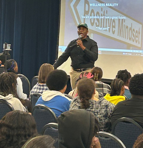 Darrell 'Coach D' Andrews speaks with a microphone to high school students seated in chairs