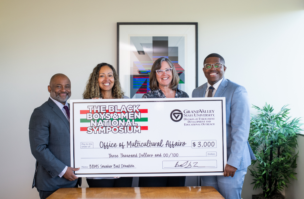 four people holding oversized check from the Black Boys and Men Symposium