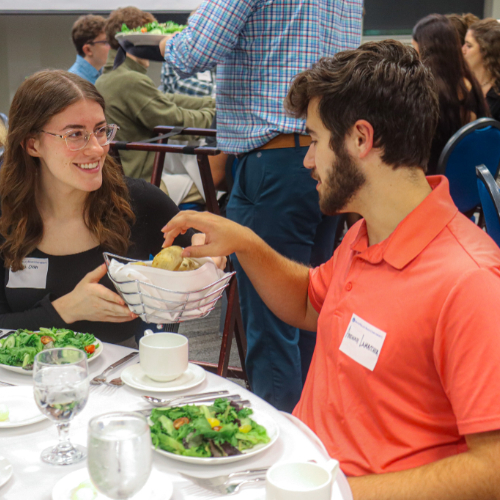 one student passes dinner rolls to her left to another student