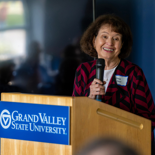 Gayle Davis holds microphone and speaks from podium with GVSU logo