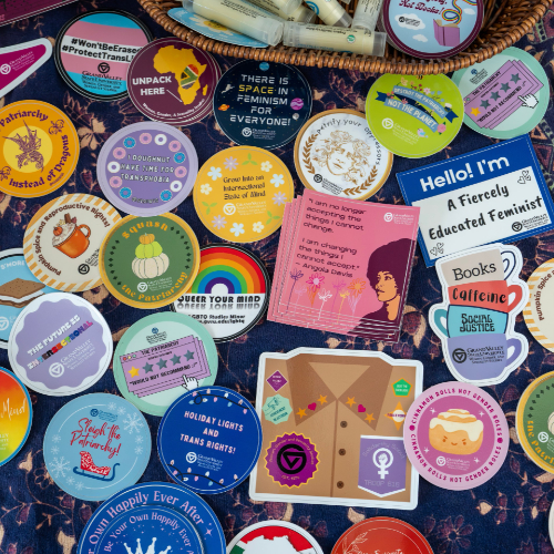 array of stickers promoting feminism and Brooks College are spread on a table