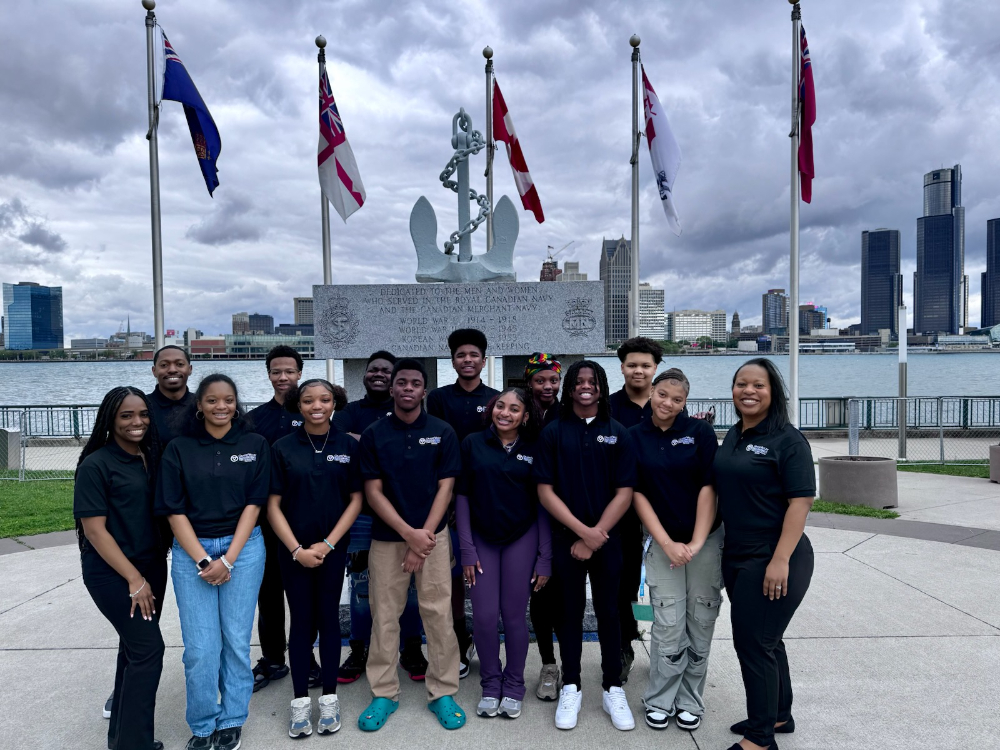 two rows of students and staff standing in front of military memorial in Windsor Canada, Detroit River and Detroit in background
