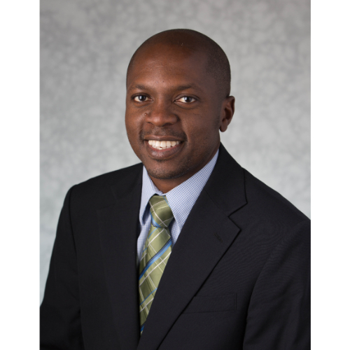 Babasola Fateye in dark suit jacket, light blue shirt with green tie with stripes