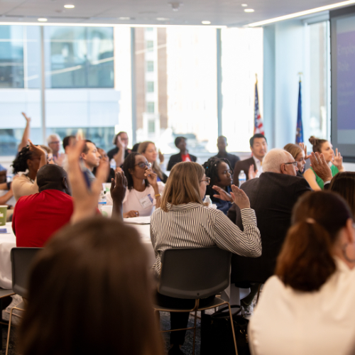 people seated at tables, some with hands raised