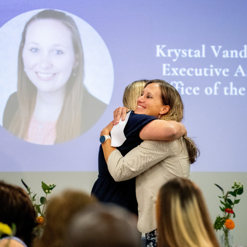 two women hugging while screen is projected in background