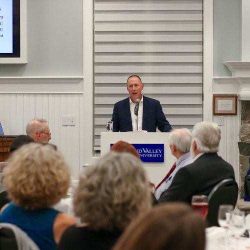 Keith Donovan speaks from a podium; people seated at tables at the Alumni House