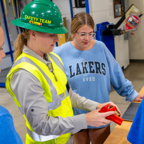 person in safety vest and hard hat in center showing device to students