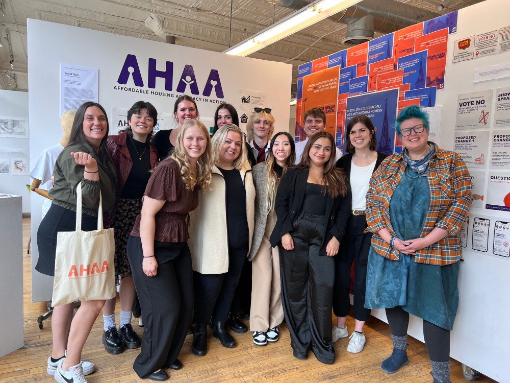 group of students, professor and staff standing in front of materials that brand AHAA, an affordable housing advocacy program. campaign materials in red and blue, posters and one student on left is holding a tote bag