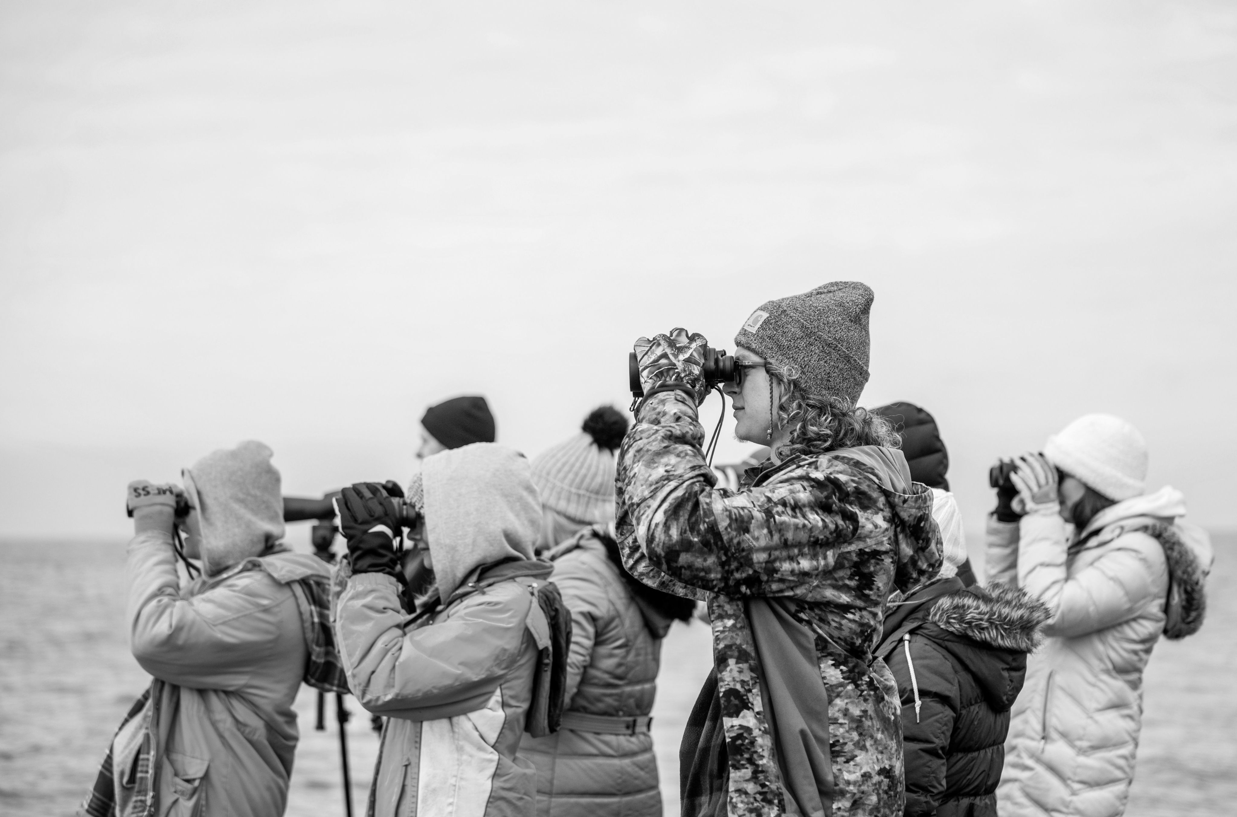 students on a boat in warm jackets, hoods and hats look through binoculars