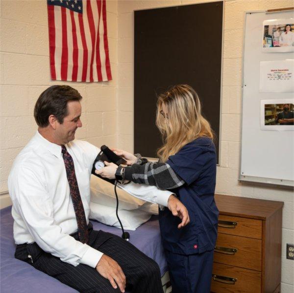 Man in white shirt gets blood pressure check from student in blue scrubs