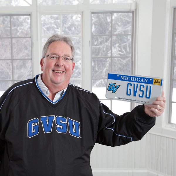 Bob Stoll holds a license plate with GVSU on it, a GVSU specialized plate