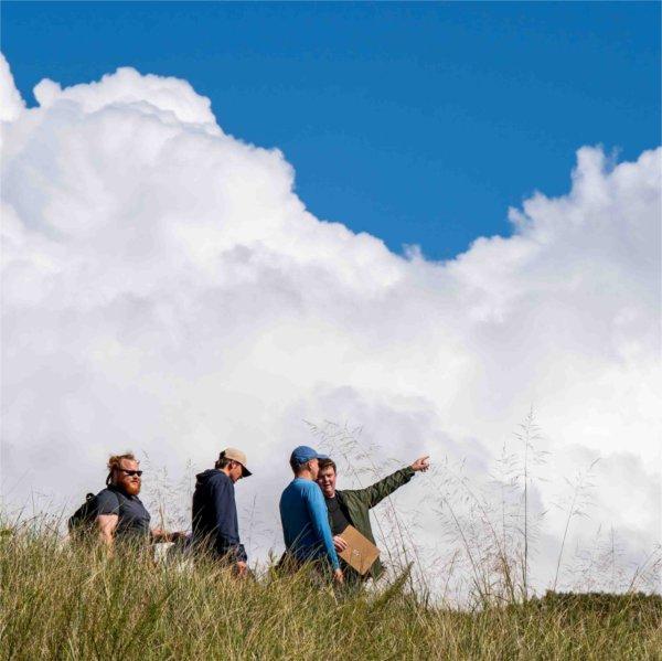 Clouds loom in the background as college students walk through tall beach grass on an outdoor classroom assignment.