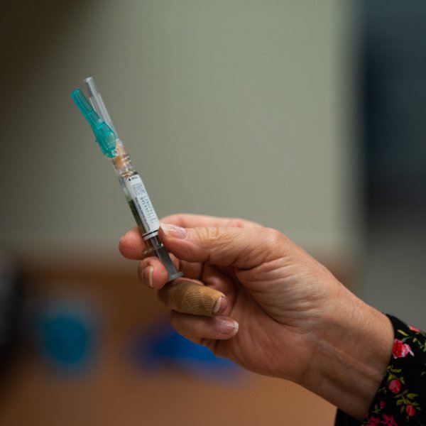 A hand holding a syringe with a flu vaccine in it