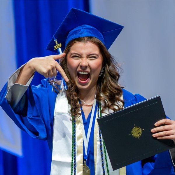 A graduate points to her diploma during a commencement ceremony.