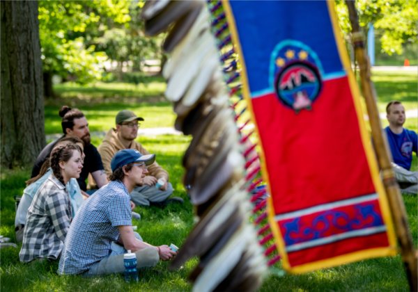 students seated in a circle, Native banner with feathers at right