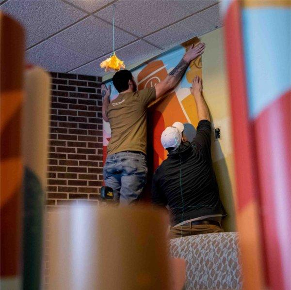 An installation worker places a strip of vinyl mural on the wall.