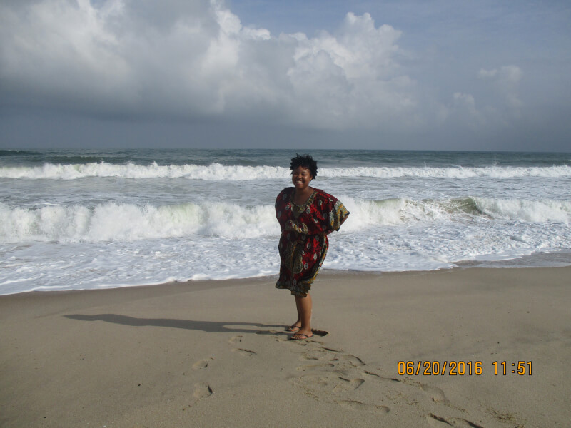 Elayne Vaugn stands on a beach next to the ocean.