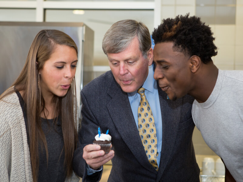  A photo of President Haas celebrating with two students.