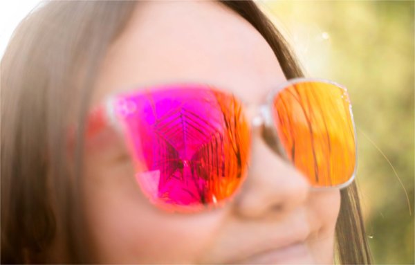  A person wearing pink and orange sunglasses smiles.