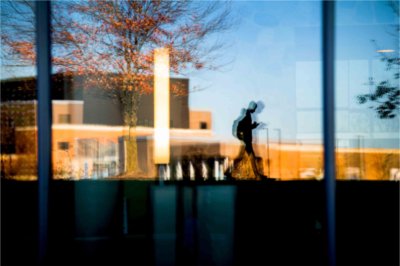 The silhouette of a student walking with their phone is reflected into glass windows.