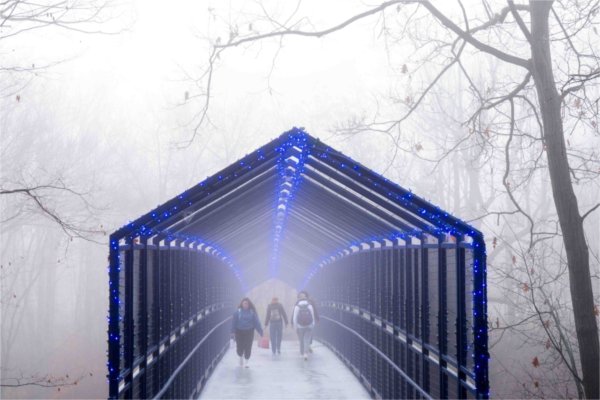 Pedestrians walk on a blue bridge in the fog. 