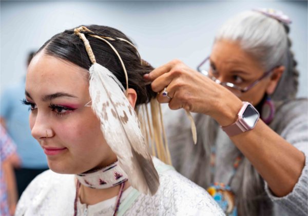  An Indigenous dancer receives help with regalia before a Powwow Ceremony.