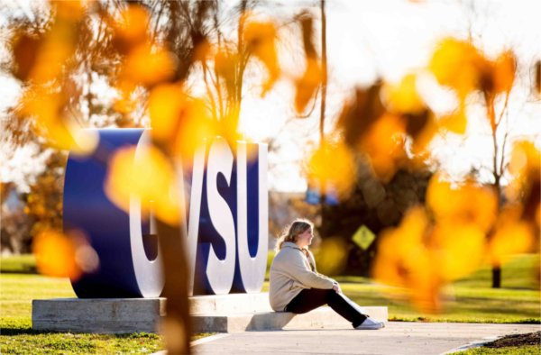  A person is pictured at the Laker Letters with yellow and orange autumn tree colors.